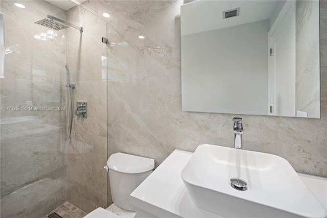 bathroom with toilet, tiled shower, decorative backsplash, vanity, and tile walls