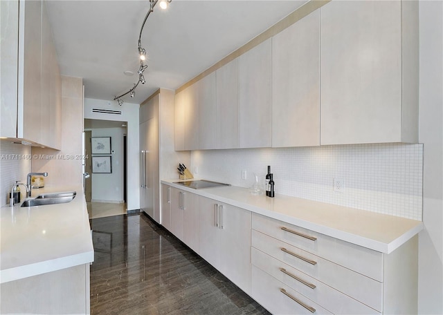 kitchen with black electric stovetop, rail lighting, sink, dark hardwood / wood-style floors, and tasteful backsplash