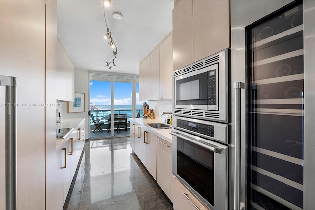 kitchen featuring decorative backsplash, stainless steel appliances, beverage cooler, sink, and a water view