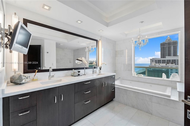 bathroom featuring vanity, a tray ceiling, a relaxing tiled tub, an inviting chandelier, and a water view