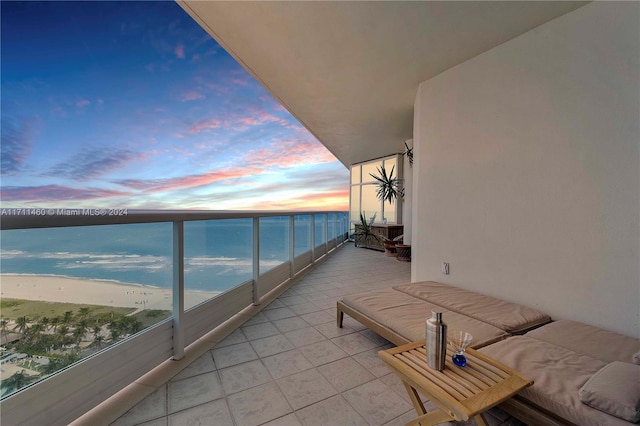 balcony at dusk featuring a water view and a view of the beach