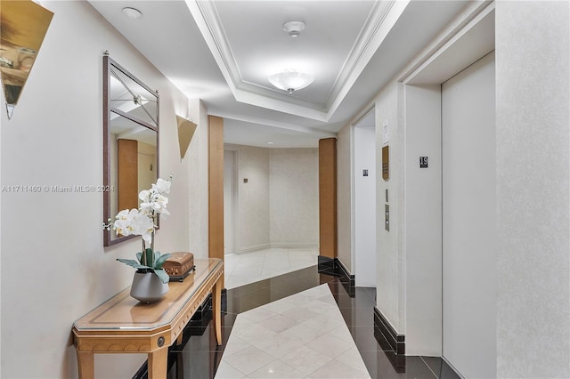 hall with elevator, a raised ceiling, dark tile patterned floors, and crown molding