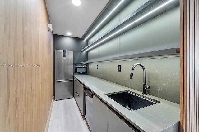 kitchen with appliances with stainless steel finishes, tasteful backsplash, light hardwood / wood-style flooring, and sink