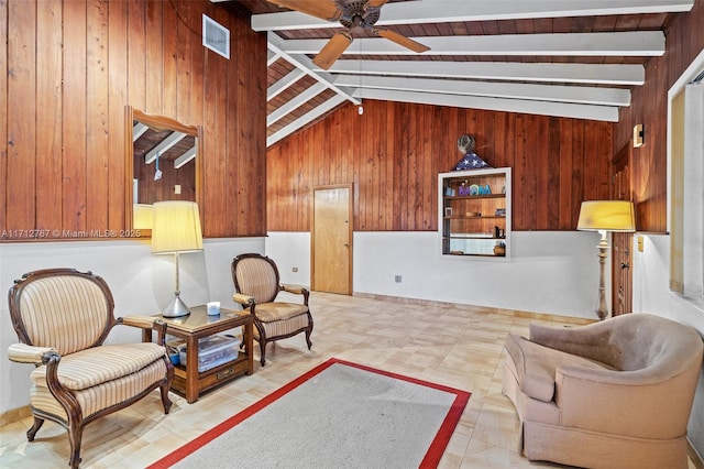 living area with wooden walls, lofted ceiling with beams, and ceiling fan