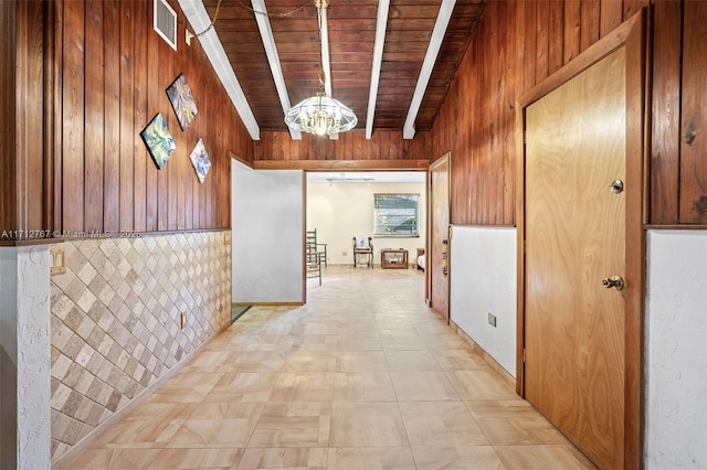 corridor with an inviting chandelier, wood ceiling, beam ceiling, and wooden walls