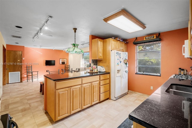 kitchen with decorative light fixtures, rail lighting, sink, dark stone countertops, and white appliances