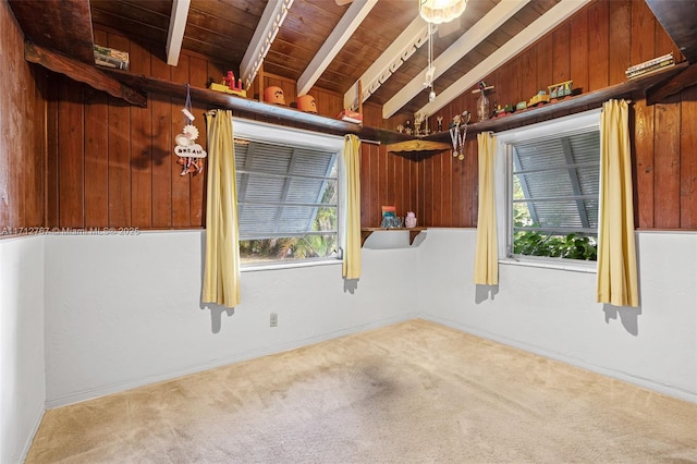 unfurnished room with a wealth of natural light, lofted ceiling with beams, wooden ceiling, and carpet