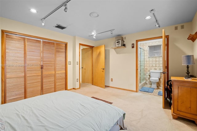 bedroom with rail lighting, ensuite bath, light colored carpet, and a closet