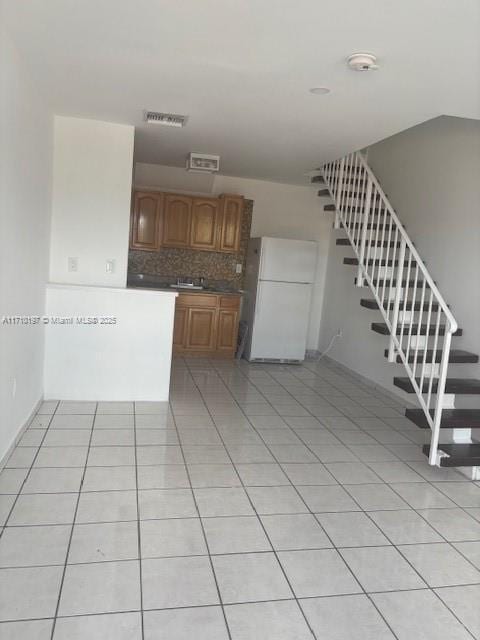 kitchen with light tile patterned floors, a sink, backsplash, freestanding refrigerator, and brown cabinetry