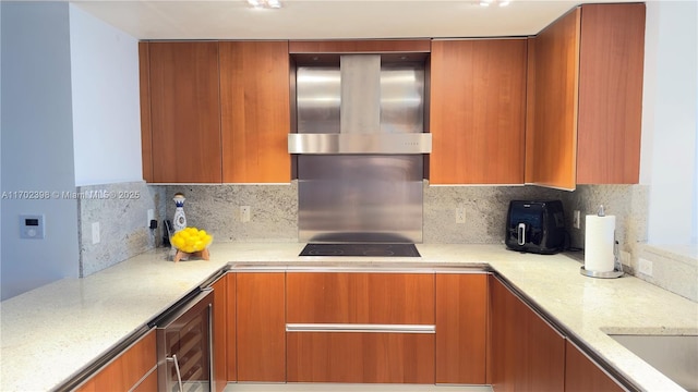 kitchen with light stone counters, wall chimney range hood, decorative backsplash, and beverage cooler