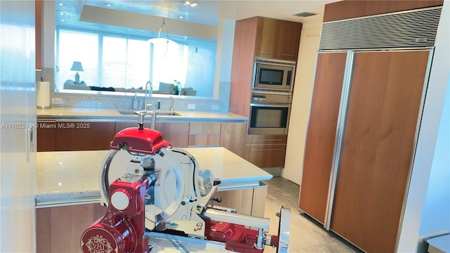 kitchen featuring sink, built in appliances, and light stone counters