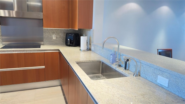 kitchen with tasteful backsplash, sink, light stone counters, wall chimney range hood, and black electric cooktop