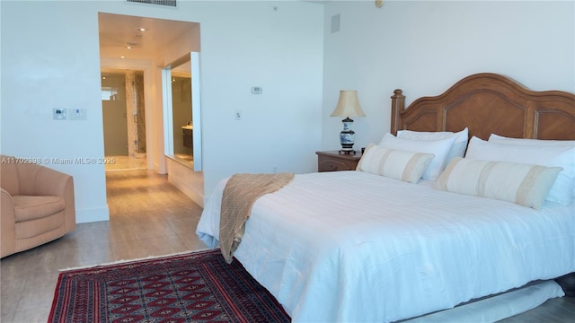 bedroom with ensuite bathroom and hardwood / wood-style floors