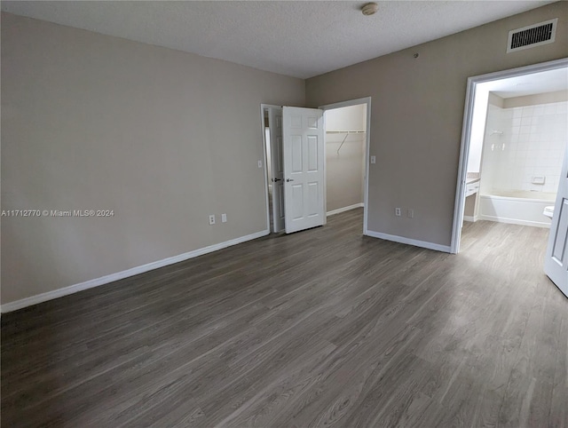 unfurnished bedroom with dark hardwood / wood-style floors, a spacious closet, a textured ceiling, connected bathroom, and a closet