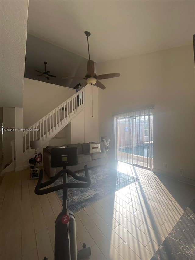 living room with ceiling fan, a towering ceiling, and light hardwood / wood-style flooring