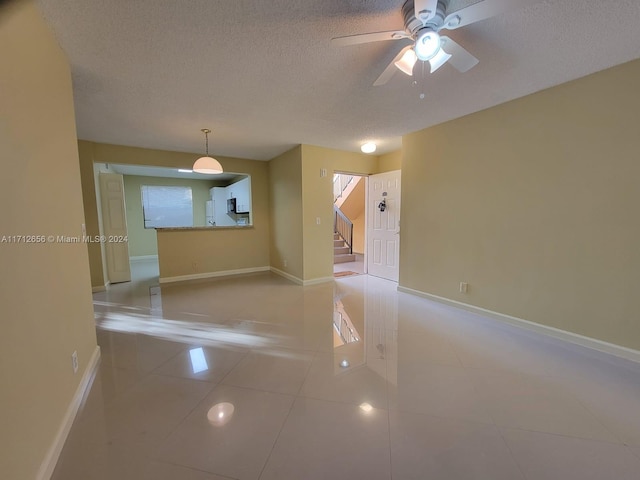 tiled empty room with ceiling fan and a textured ceiling