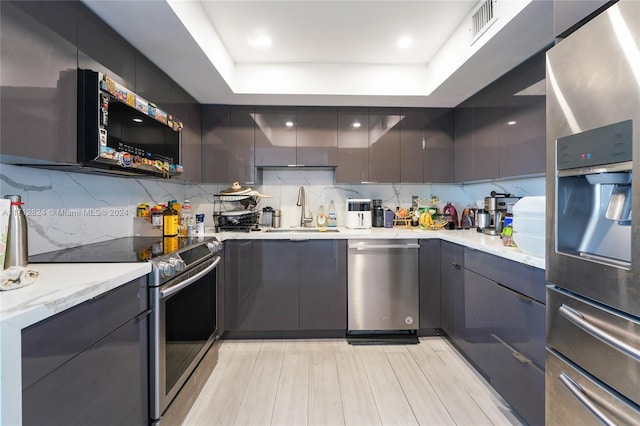 kitchen with a raised ceiling, sink, stainless steel appliances, and tasteful backsplash