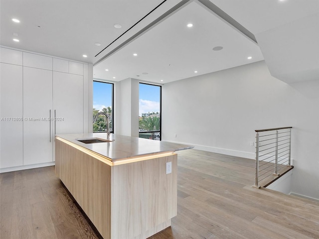 kitchen featuring sink, a large island with sink, light brown cabinets, light hardwood / wood-style flooring, and white cabinets