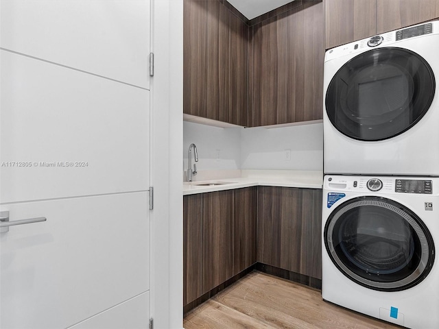 laundry room with light hardwood / wood-style floors, cabinets, sink, and stacked washer and clothes dryer