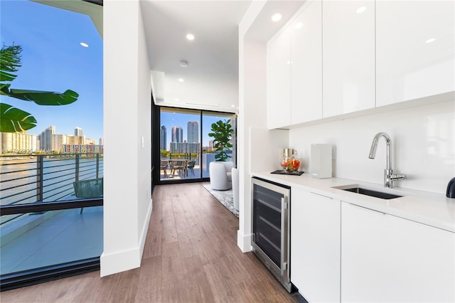 bar featuring floor to ceiling windows, white cabinets, sink, hardwood / wood-style flooring, and beverage cooler