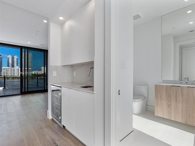 kitchen with light hardwood / wood-style floors, white cabinetry, sink, and beverage cooler