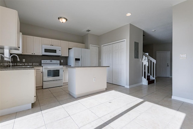 kitchen with tasteful backsplash, white appliances, sink, a kitchen island, and light tile patterned flooring