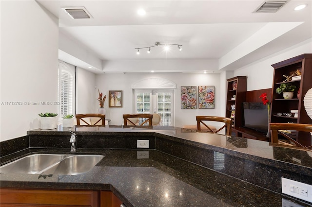 kitchen featuring a raised ceiling, dark stone countertops, and sink