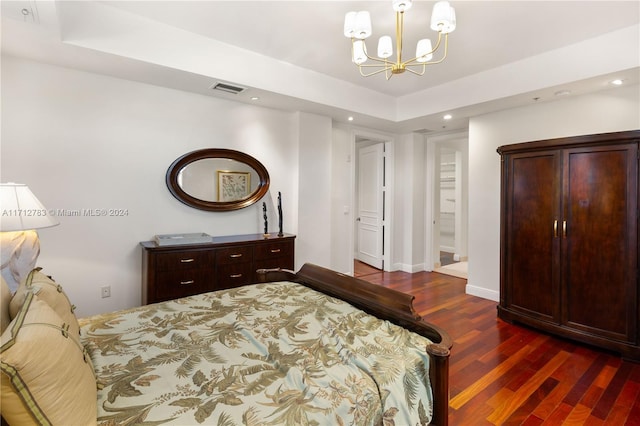 bedroom with a raised ceiling, dark hardwood / wood-style flooring, and an inviting chandelier