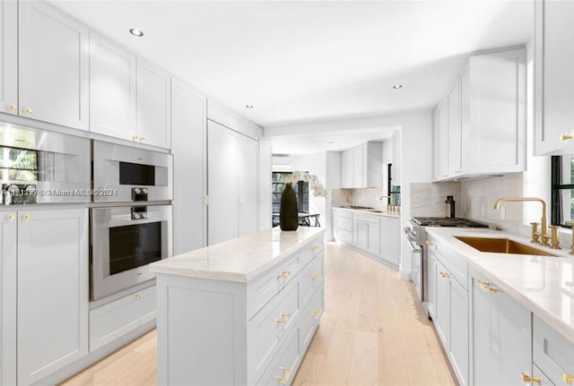 kitchen featuring light stone countertops, sink, tasteful backsplash, light hardwood / wood-style flooring, and white cabinets