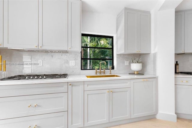 kitchen featuring sink, stainless steel gas cooktop, light hardwood / wood-style floors, decorative backsplash, and white cabinets