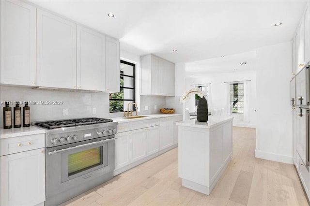 kitchen featuring white cabinetry, sink, tasteful backsplash, light hardwood / wood-style floors, and stainless steel stove