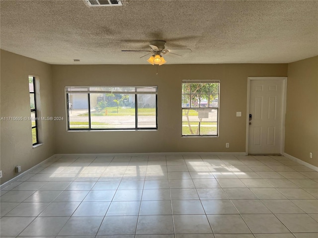 empty room featuring ceiling fan, plenty of natural light, light tile patterned flooring, and a textured ceiling