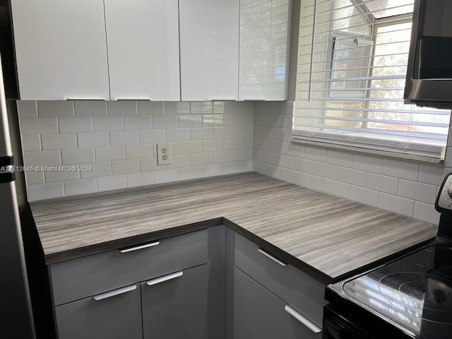 kitchen featuring tasteful backsplash, stainless steel refrigerator, white cabinetry, and black / electric stove