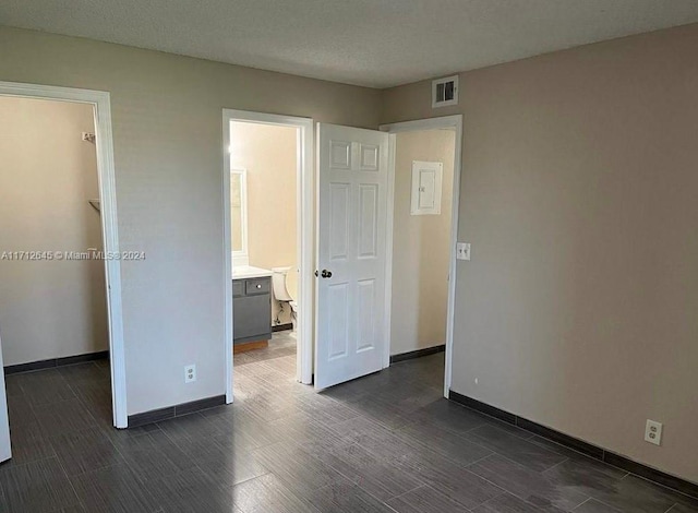 unfurnished bedroom featuring a textured ceiling, a walk in closet, ensuite bath, and dark hardwood / wood-style floors