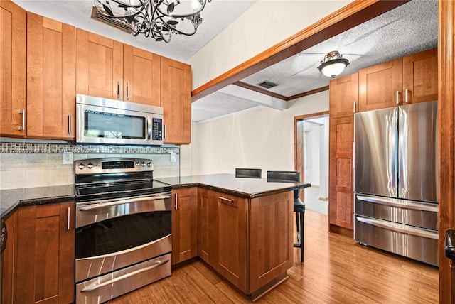 kitchen featuring decorative backsplash, appliances with stainless steel finishes, kitchen peninsula, an inviting chandelier, and light hardwood / wood-style floors