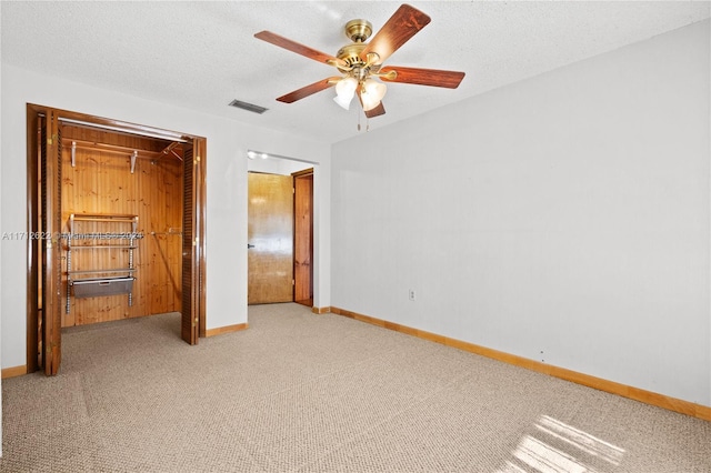 unfurnished bedroom with ceiling fan, light colored carpet, a textured ceiling, wooden walls, and a closet