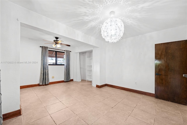 tiled spare room with ceiling fan with notable chandelier