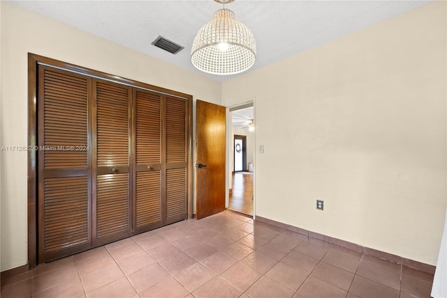 unfurnished bedroom with a closet, tile patterned flooring, and an inviting chandelier