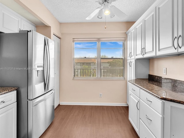 kitchen featuring ceiling fan, stainless steel refrigerator with ice dispenser, dark stone countertops, white cabinets, and light wood-type flooring