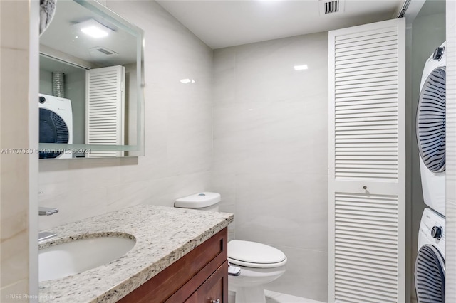 bathroom with vanity, toilet, stacked washing maching and dryer, and tile walls