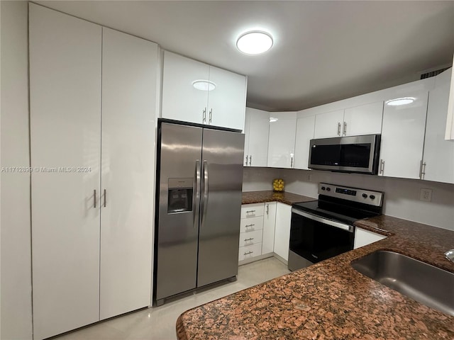 kitchen featuring white cabinets, appliances with stainless steel finishes, dark stone counters, and sink