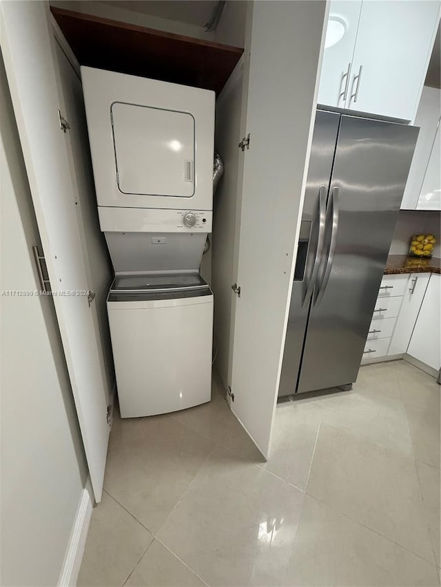 clothes washing area featuring light tile patterned floors and stacked washer and clothes dryer