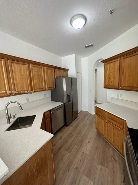 kitchen featuring a textured ceiling, light wood-type flooring, stainless steel appliances, and sink