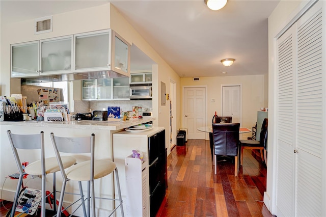 kitchen with white cabinets, dark hardwood / wood-style floors, backsplash, and a breakfast bar area