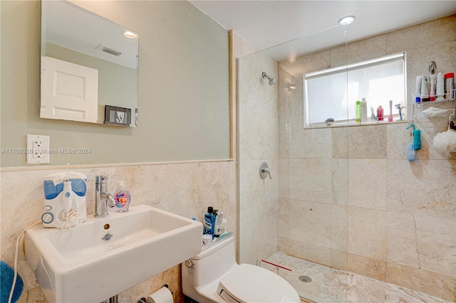 bathroom featuring tiled shower, toilet, tile walls, and sink