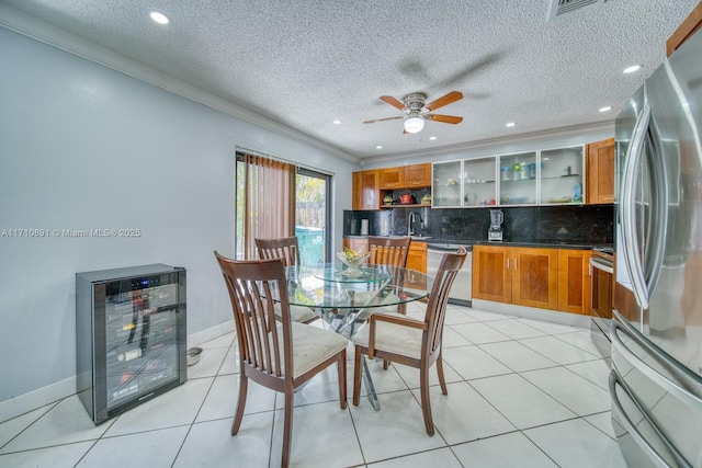 tiled dining area featuring sink, crown molding, beverage cooler, and a textured ceiling