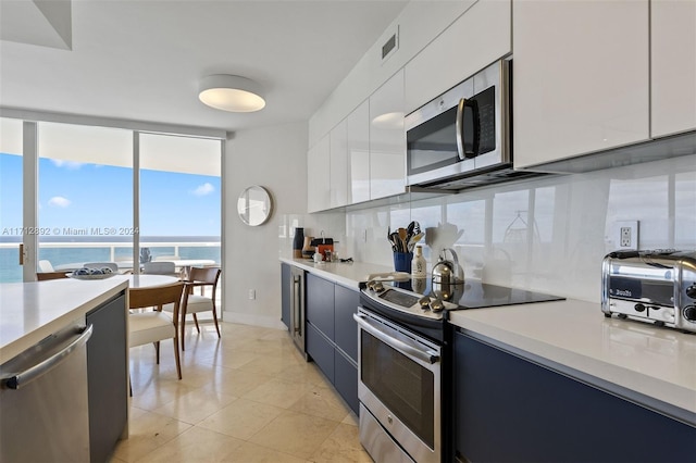 kitchen featuring tasteful backsplash, stainless steel appliances, a water view, white cabinets, and light tile patterned flooring