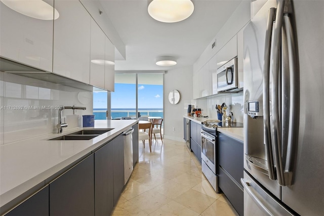 kitchen with sink, stainless steel appliances, a water view, decorative backsplash, and white cabinets