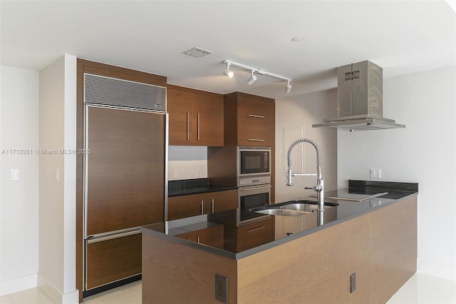 kitchen with dark countertops, visible vents, a sink, ventilation hood, and built in appliances