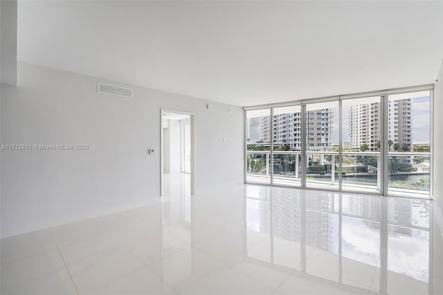 unfurnished room featuring a wall of windows, light tile patterned floors, a healthy amount of sunlight, and visible vents